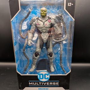 Puede incluir: Una figura de acción de Brainiac de DC Multiverse en un paquete de plástico transparente. La figura es gris y plateada con una cabeza verde y detalles en rosa. El embalaje incluye el logotipo de DC y el texto "Brainiac".