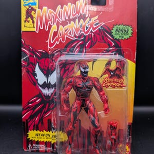 May include: A Maximum Carnage action figure in its original packaging. The figure is red with black accents and comes with a weapon accessory. The packaging is red and yellow with the Marvel Comics logo and the words "Maximum Carnage".