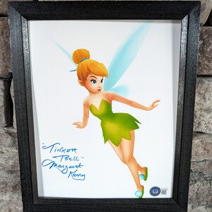 May include: Framed artwork of Tinker Bell in a green dress and blue wings, with a signature and the text "Tinker Bell" and "Margaret Kerry". The black framed artwork is displayed against a stone wall.