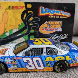 Op de afbeelding: Een 1/24 schaal diecast auto van de #30 America Online raceauto met het Looney Tunes-personage Daffy Duck. De auto is blauw, wit en geel met het AOL-logo en het nummer 30 aan de zijkant. De auto staat op een blauwe ondergrond.
