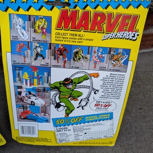 May include: A vintage Marvel Super Heroes action figure package. The packaging features illustrations of Silver Surfer, Hulk, Spider-Man, Punisher, Daredevil, Dr. Doom, Captain America, and Dr. Octopus. The package has a blue and yellow design with the Marvel logo.
