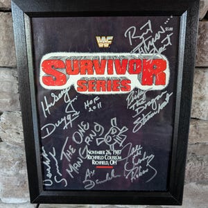 May include: Framed poster for the WWF Survivor Series event. The poster features the event title in red and white, surrounded by signatures. The event date and location, November 26, 1987, Richfield Coliseum, OH, are also visible.