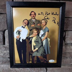 Könnte beinhalten: Ein gerahmtes Foto mit vier Personen in Vintage-Kleidung vor beigem Hintergrund. Zu sehen sind ein Mann im Smoking, ein Mann im Tweed-Anzug, eine Frau im Rockkostüm und eine Frau im grauen Kleid mit Schürze. Der Druck enthält eine handschriftliche Signatur und einen JSA-Authentifizierungsaufkleber.