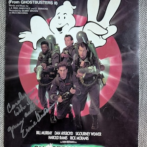 May include: A sheet music cover for the song "On Our Own" from the movie "Ghostbusters II". The cover features a cartoon ghost with a mischievous grin and the four main actors from the film: Bill Murray, Dan Aykroyd, Sigourney Weaver, Harold Ramis, and Rick Moranis. The cover is signed by Ernie Hudson.