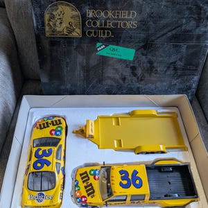 Op de afbeelding: Een gele M&M's raceauto- en vrachtwagen set met het nummer 36 op de zijkanten. De set bevat een gele aanhanger. De doos is gemarkeerd met "Brookfield Collectors Guild" en heeft een "QVC" inspectiesticker.