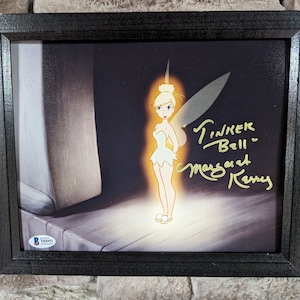 May include: Framed artwork of Tinker Bell from Disney's Peter Pan, with a gold signature reading "Tinker Bell" and "Margaret Kerry". The image is set against a dark background and enclosed in a black frame.