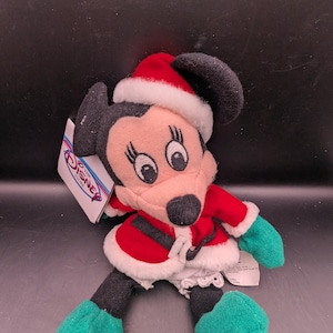 K&ouml;nnte beinhalten: Ein Pl&uuml;sch Minnie Mouse-Puppe in einem Weihnachtsmann-Outfit. Die Puppe hat einen rot-wei&szlig;en Weihnachtsmannhut, einen roten Mantel mit wei&szlig;em Besatz und gr&uuml;ne Handschuhe und Schuhe. Das Disney Store-Etikett ist angebracht.