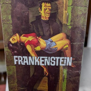 Peut inclure: Une boîte vintage pour un kit de modèle en plastique de Frankenstein. La boîte présente une illustration colorée de Frankenstein portant une femme dans ses bras. Le texte sur la boîte indique "Moebius Monster Scenes All Plastic Snap Together Custom Builder Kits Frankenstein".