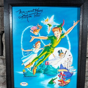 May include: Framed artwork featuring Peter Pan and other characters from the animated film. The artwork is signed by Margaret Kerry, who voiced Tinker Bell. The image has a blue background with a black frame.