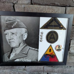 Peut inclure: Cadre noir contenant un portrait en noir et blanc d'un officier militaire en uniforme, avec des écussons et insignes militaires. Le cadre est rectangulaire. Fond en pierre.