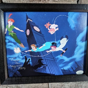 May include: A framed print of a scene from the film Peter Pan, featuring Peter Pan, Wendy Darling, John Darling, and Captain Hook flying over London. The print is signed by the artists,  "Pinoc Bell" and "Margaret  Kenny".