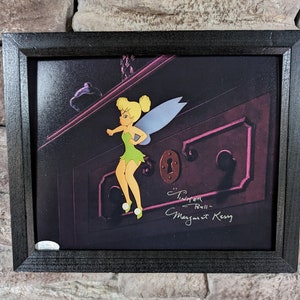 May include: A framed illustration of Tinker Bell, a fairy from the Disney movie Peter Pan, flying in front of a dark wooden cabinet door. The illustration is signed "Tinker Bell" and "Margaret Kerry".