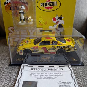 Op de afbeelding: Een gele 1:24 schaal diecast replica van de 2001 Pennzoil/Looney Tunes Chevrolet Monte Carlo, bestuurd door Steve Park en Looney Tunes. De auto wordt getoond in een transparante kunststof vitrine met een certificaat van echtheid. Het certificaat vermeldt dat de figuur een van de 5.790 stuks is.