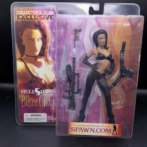 Puede incluir: Figura de acción Hellspawn Biker Chick en un embalaje de plástico transparente. La figura viste ropa negra y tiene un arma. El embalaje incluye el texto "COLLECTOR'S CLUB EXCLUSIVE" y "SPAWN.COM".