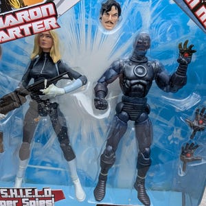 Puede incluir: Un set de figuras de acci&oacute;n Marvel Legends que incluye a Iron Man con un traje sigiloso y a Sharon Carter, una superesp&iacute;a de S.H.I.E.L.D. Las figuras est&aacute;n empaquetadas en un bl&iacute;ster de pl&aacute;stico transparente con fondo azul y blanco. El empaque incluye el logotipo de Marvel Legends y el texto "Stealth Iron Man" y "S.H.I.E.L.D. Super Spies!"