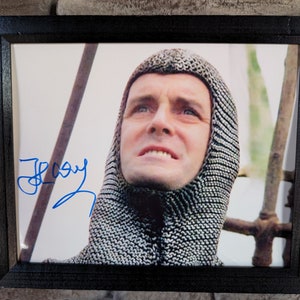 Può includere: Una foto in bianco e nero di un uomo con un cappuccio di maglia a catena, che guarda in alto. La foto è firmata "Gary" con inchiostro blu.