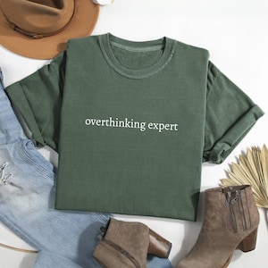 May include: A green t-shirt with the text "overthinking expert" printed in white on the front.