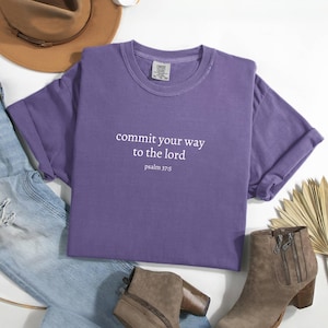 May include: Purple t-shirt with the text "commit your way to the lord psalm 37:5" printed in white.