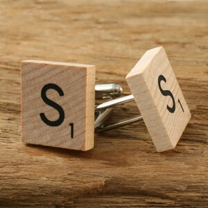 May include: Cufflinks with wooden tiles displaying the letter "S" and the number "1" in black. The cufflinks have a silver metal backing. The wooden tiles are displayed on a wooden surface.