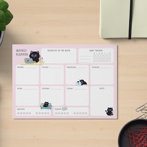 May include: A pink weekly planner with a cat theme. The planner includes sections for each day of the week, priorities, and a habit tracker. The planner has illustrations of black cats engaging in various activities.