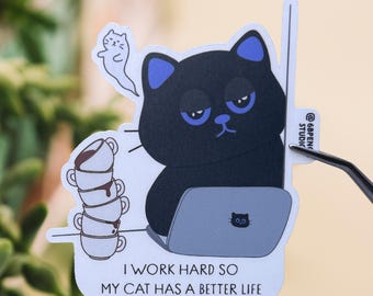 May include: A black cat with blue ears sits at a laptop computer with a stack of coffee cups behind it. The text reads "I work hard so my cat has a better life."