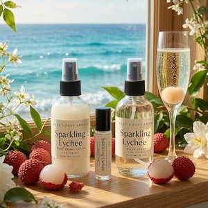 May include: Two clear 4 oz. spray bottles and one small roller bottle labeled Gulf Coast Aromas Sparkling Lychee. The bottles are arranged on a wooden ledge with fresh lychee fruit and a glass of sparkling liquid against an ocean backdrop.