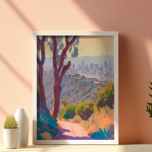 May include: A framed painting depicting a city skyline viewed from a hillside with a dirt road leading up to the trees. The trees are a deep red colour and the city is a hazy blue in the distance.