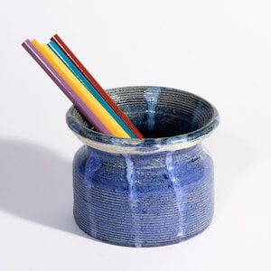Puede incluir: Un porta lápices de cerámica azul con una superficie texturizada y un arcoíris de lápices de colores que sobresalen de la parte superior.