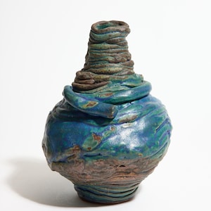 Puede incluir: Un jarrón de cerámica hecho a mano con un diseño orgánico y texturizado. El jarrón presenta una base bulbosa y una parte superior cilíndrica en espiral. La paleta de colores incluye tonos de azul, verde y marrón.