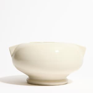 Puede incluir: Juego de mortero y mano de cerámica de color crema. El mortero tiene un cuenco ancho y redondeado con una pequeña boquilla a cada lado. La base es un pedestal corto y circular. El pilón no es visible.