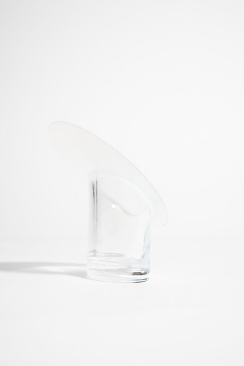 May include: A clear glass with a curved, frosted glass accent. The glass has a cylindrical shape with a rounded base. The frosted accent extends from the top, creating a unique, modern design. The glass is set against a white background.