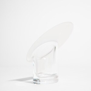May include: A clear glass object with a cylindrical base and a curved, oval-shaped top. The object is transparent, allowing light to pass through. The design is minimalist and modern, set against a white background.
