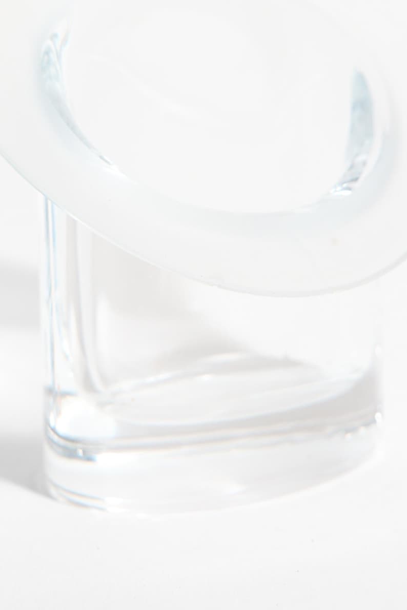 May include: A clear glass container with a rounded top and a square base. The glass is transparent, allowing light to pass through. The design is minimalist and modern, suitable for various uses.