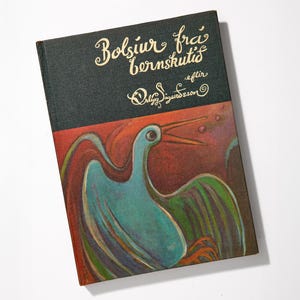 May include: A hardcover book titled "Bolsiur frá bernskutíð" with a teal bird illustration on the cover. The book has a dark green top and a red and orange background. The title and author's name are in gold script.