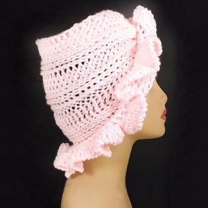 Side angle of the pink crochet ruffle hat on a mannequin, highlighting the detailed ruffles and Mobius twist that adds a touch of uniqueness to the design