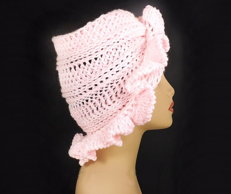 Side angle of the pink crochet ruffle hat on a mannequin, highlighting the detailed ruffles and Mobius twist that adds a touch of uniqueness to the design