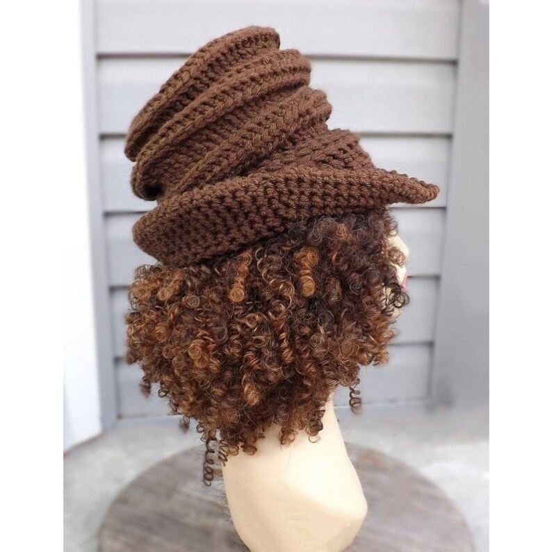 A side view of a brown crocheted hat with a swirled, ribbed texture on a mannequin head. The hat sits tall on the head and has tight curls hanging down the back.