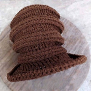 A close-up view of a crocheted brown hat lying flat. The hat has a textured, ribbed pattern and is made of thick brown yarn.