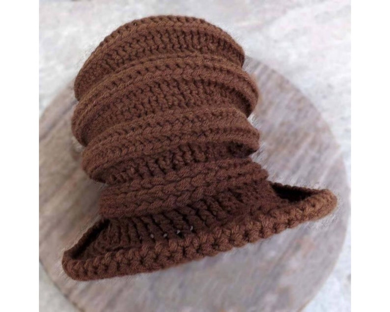 A close-up view of a crocheted brown hat lying flat. The hat has a textured, ribbed pattern and is made of thick brown yarn.