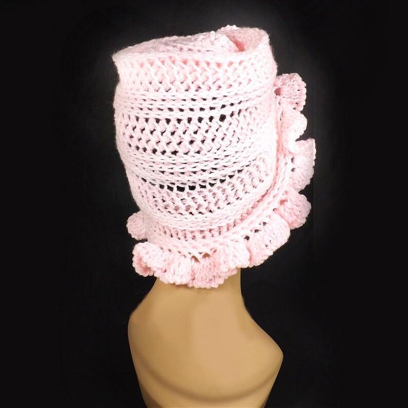 The back view of the pink crochet ruffle hat, displaying the full cascade of layered petals and the distinct Mobius twist, on a mannequin head.