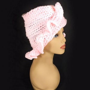 side view of the pink crochet ruffle hat worn by a mannequin, emphasizing the layered petal details and the graceful flow of the Mobius twist