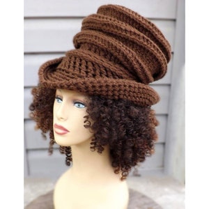 A brown crocheted hat with a ribbed, swirled pattern. The hat has an oversized, slouchy fit. The mannequin has thick curly hair.