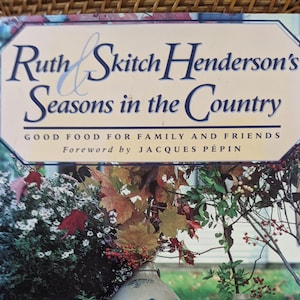 May include: A book titled "Ruth & Skitch Henderson's Seasons in the Country: Good Food for Family and Friends" with a foreword by Jacques Pépin. The cover features a still life of three blue and white painted crocks with fall foliage and berries.