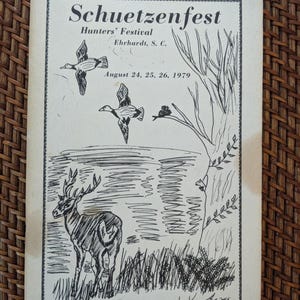 May include: A vintage black and white illustration of a Schuetzenfest Hunters' Festival poster. The artwork depicts flying ducks, a deer, and a tree near a body of water. The poster includes the date August 24, 25, 26, 1979, and the price $1.00.