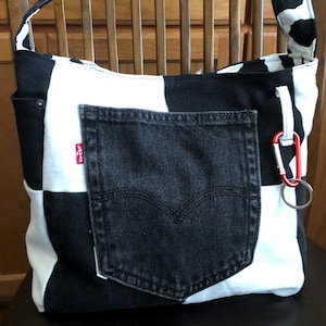 Peut inclure: Sac fourre-tout à carreaux noirs et blancs avec une grande poche en jean noir et une étiquette Levi's rouge. Le sac a une bandoulière à imprimé vache noir et blanc.