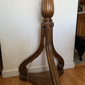May include: A wooden floor lamp with a fluted column and a three-legged base. The base has a carved design and the lamp is in a vintage style.