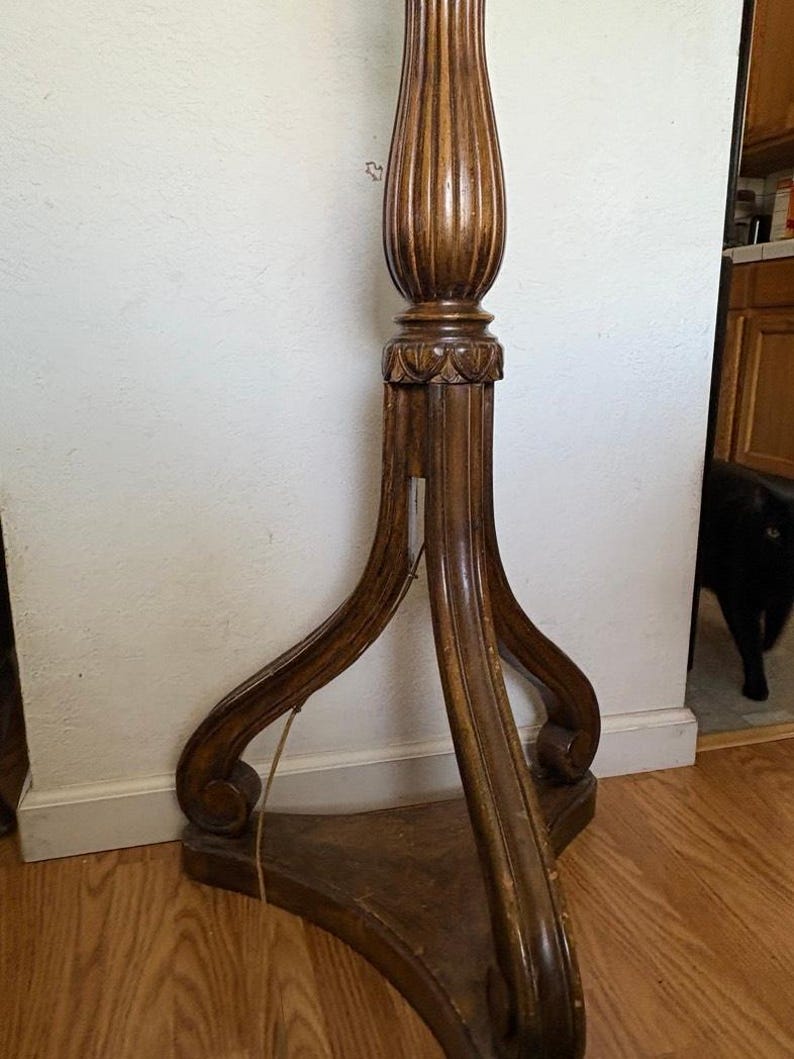 May include: A wooden floor lamp with a fluted column and a three-legged base. The base has a carved design and the lamp is in a vintage style.