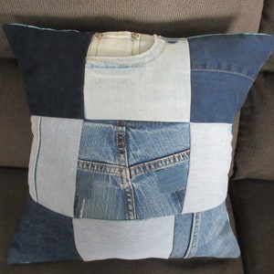 Puede incluir: Una almohada cuadrada de mezclilla con un diseño de patchwork. La almohada está hecha de diferentes tonos de mezclilla azul y presenta un bolsillo trasero en uno de los paneles.