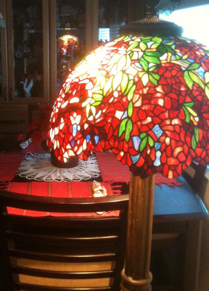 May include: A stained glass floor lamp with a red, green, and blue floral design. The lamp is on a wooden base and has a white doily on the table below it.