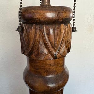 May include: A tall, wooden lamp base with a carved design. The base is dark brown and has a fluted column. The lamp has a chain for adjusting the height of the shade.